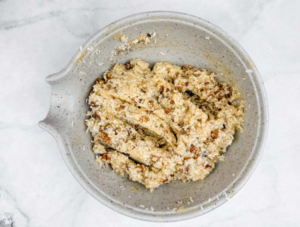 Creamy coconut rice pudding with toasted coconut flakes and nuts, served in a rustic ceramic bowl. Perfect comfort food dessert.