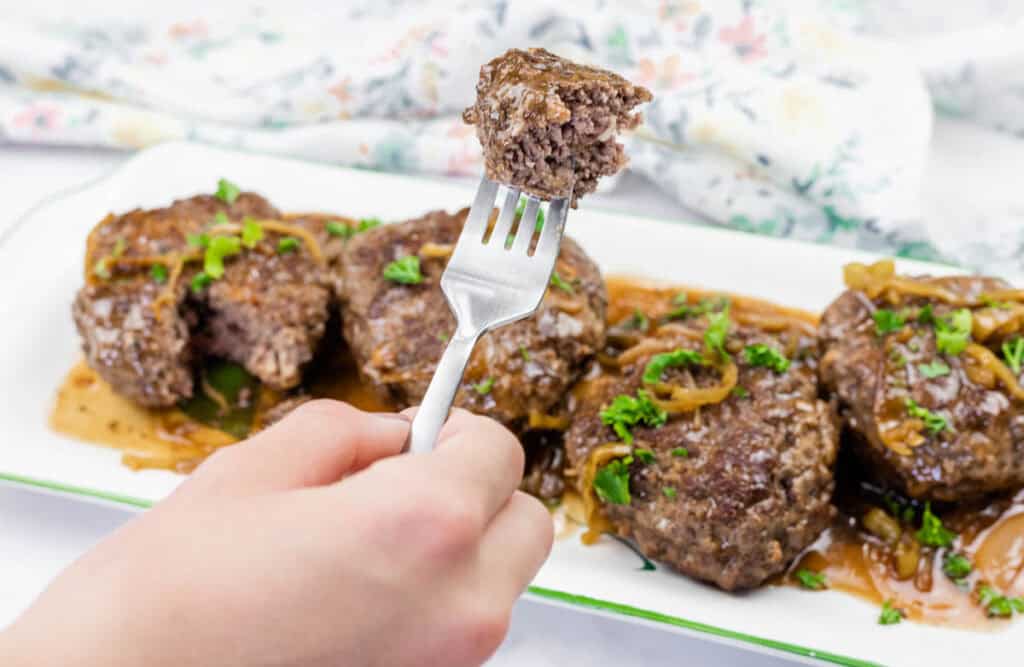 A hand holds a fork with a piece of Mississippi Salisbury steak on it.