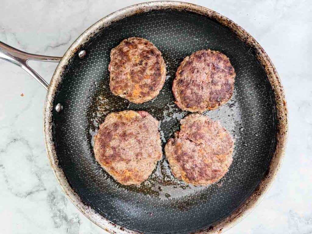 Four patties frying in the skillet.