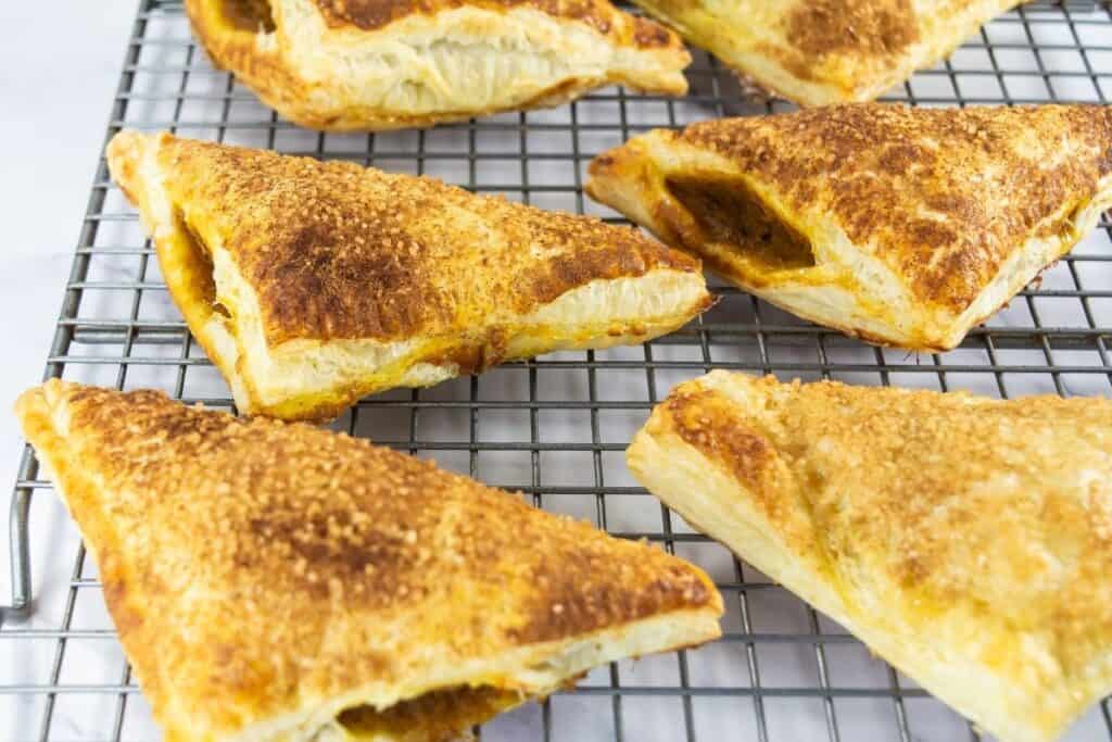 Pumpkin turnovers are cooling on a wire rack, golden and flaky with sugar topping.