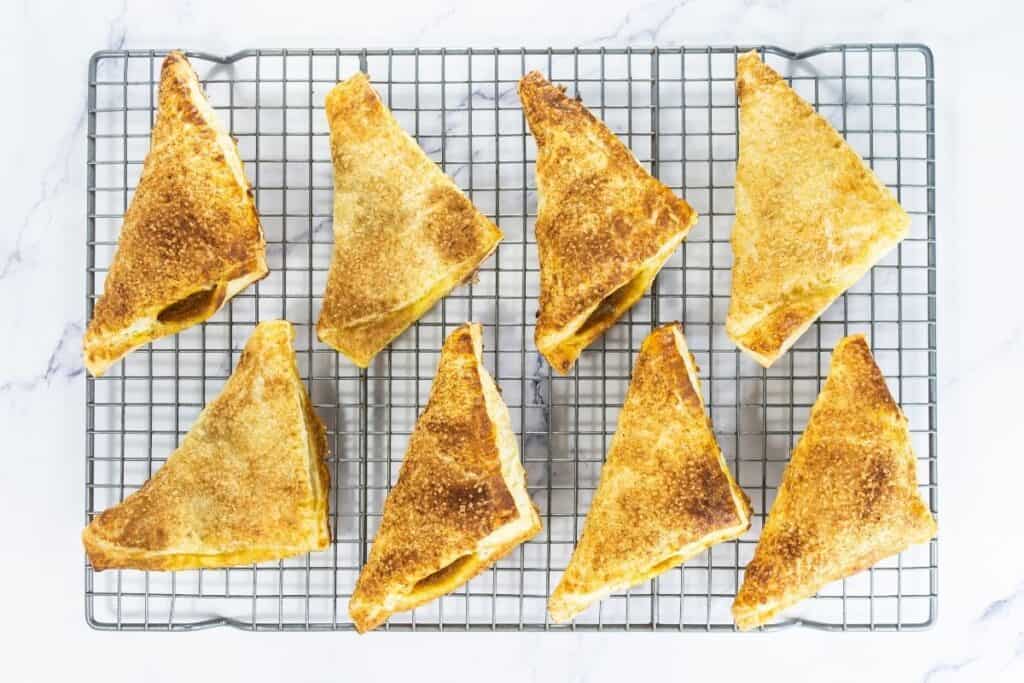 Baked pumpkin turnovers cooling on a wire rack, golden and flaky with sugar topping.