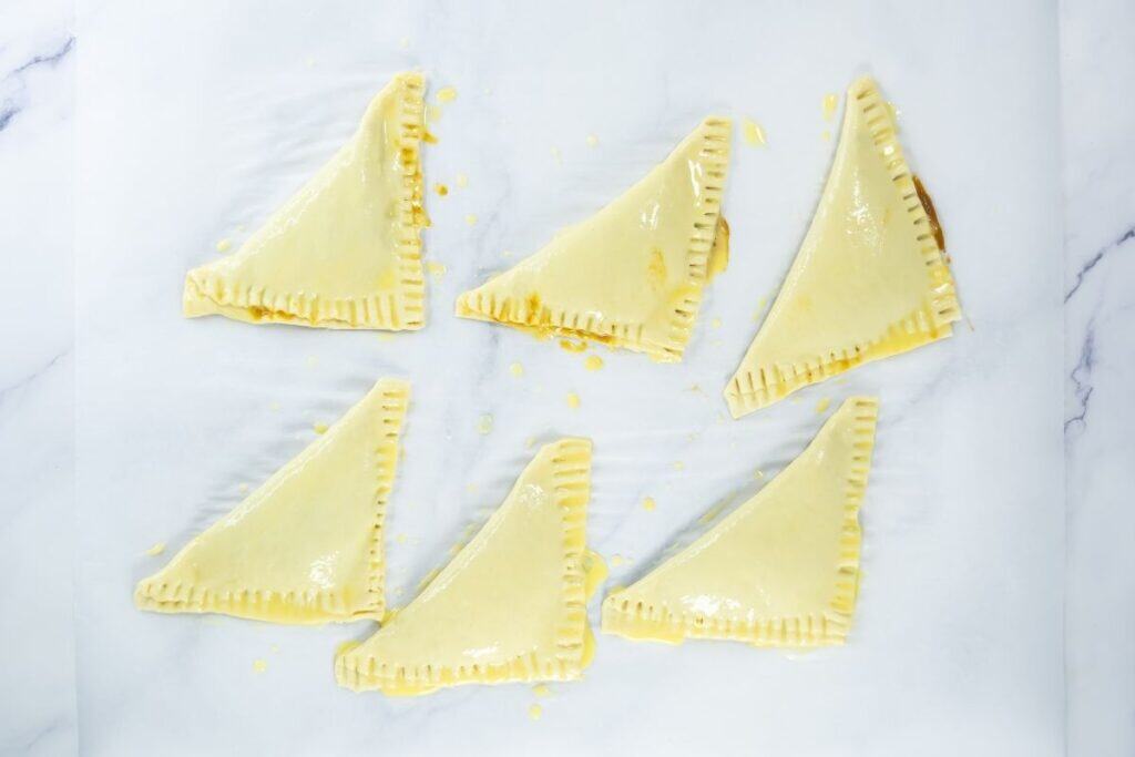 Unbaked pumpkin turnovers brushed with egg on parchment paper.