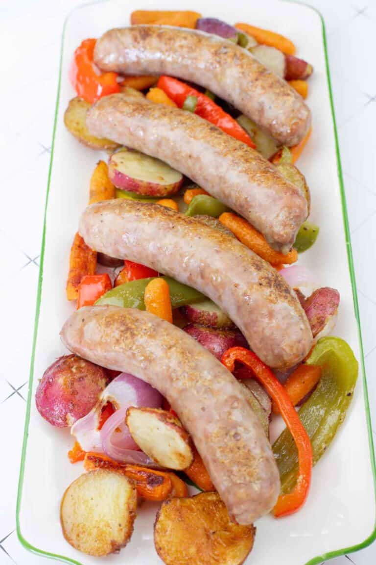 Roasted bratwurst sausages served on a platter with potatoes, carrots, peppers, and onions.