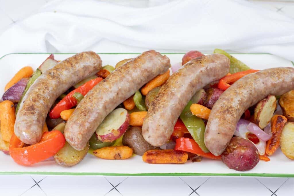 Roasted bratwurst with potatoes, carrots, and peppers arranged on a serving platter.