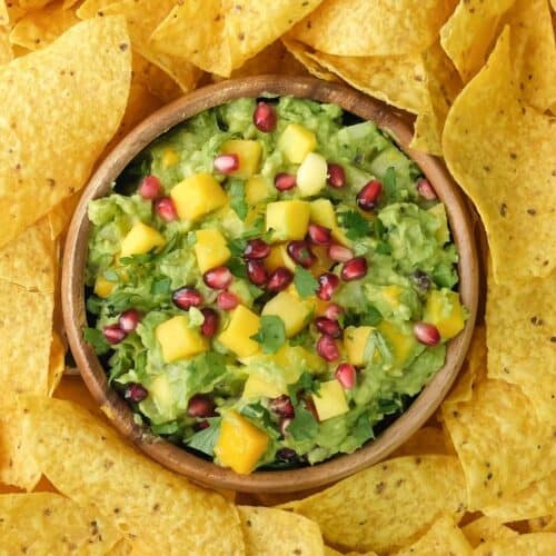 A bowl of tropical mango guacamole surrounded by nachos.