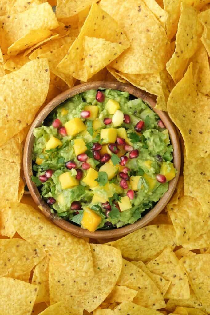 A bowl of tropical mango guacamole surrounded by nachos.
