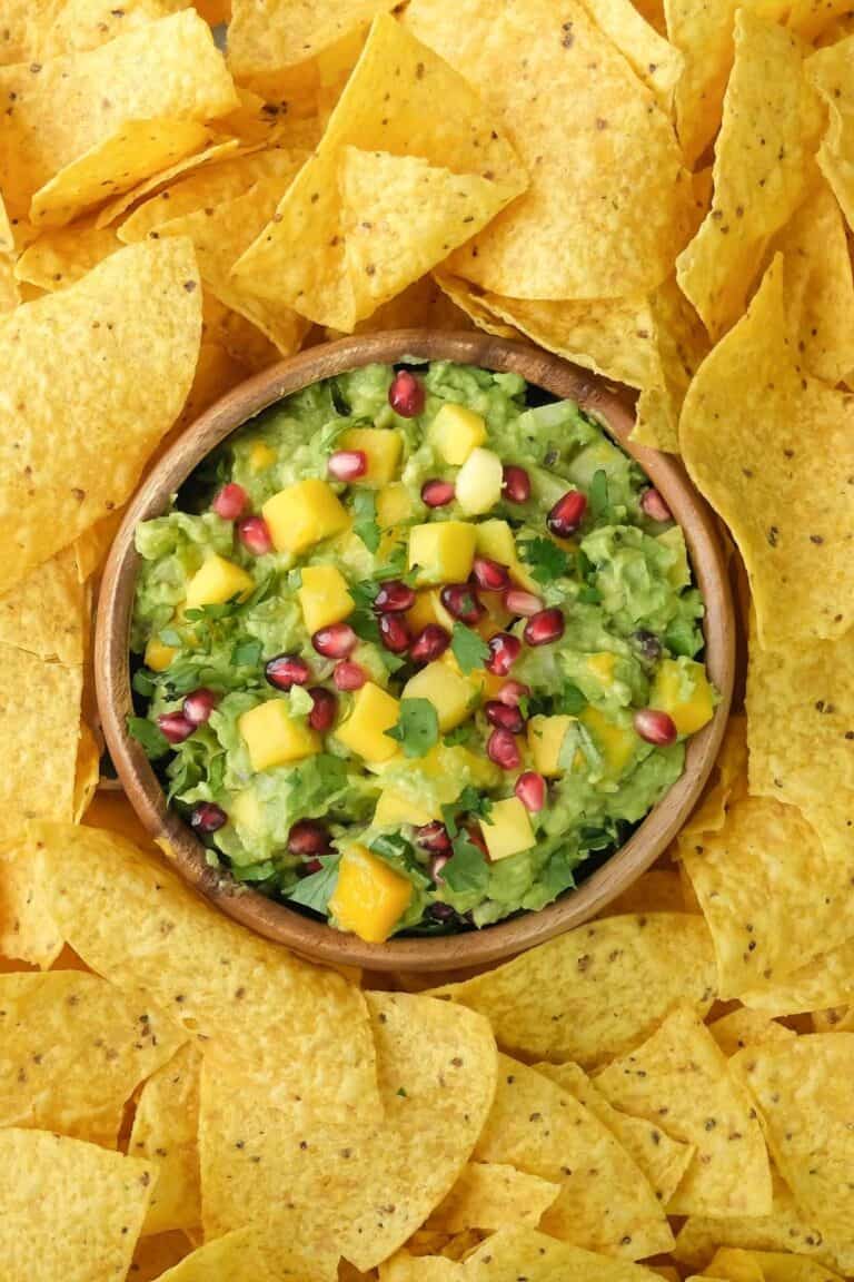 A bowl of tropical mango guacamole surrounded by nachos.