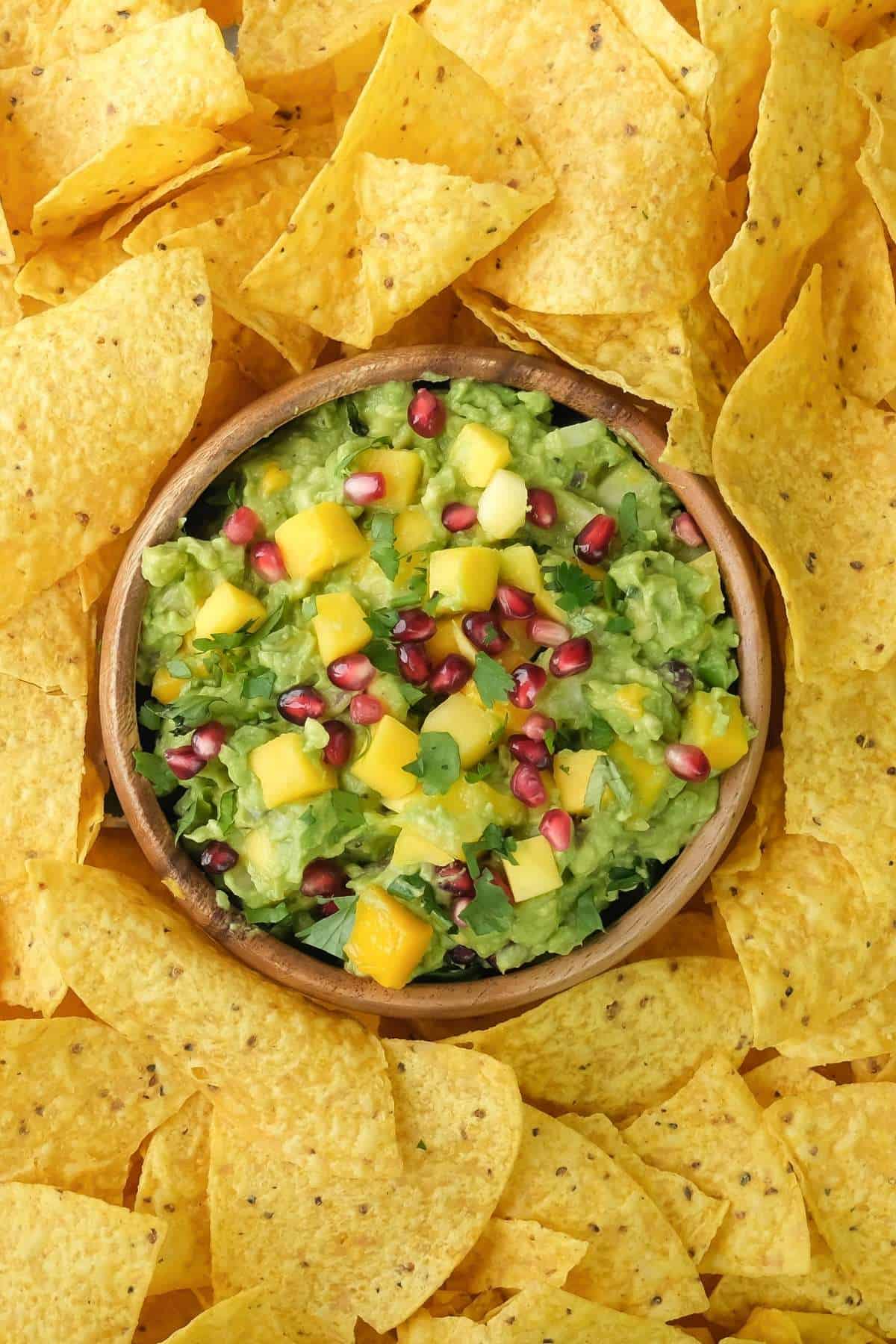 A bowl of tropical mango guacamole surrounded by nachos.