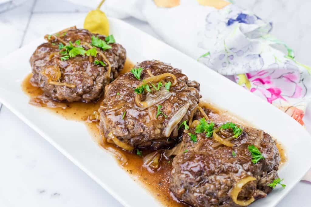Three pieces of Mississippi Salisbury Steak topped with chopped fresh parsley on a white platter.