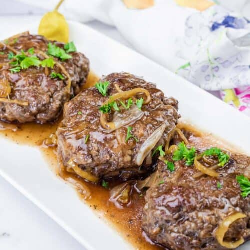 Three pieces of Mississippi Salisbury Steak topped with chopped fresh parsley on a white platter.