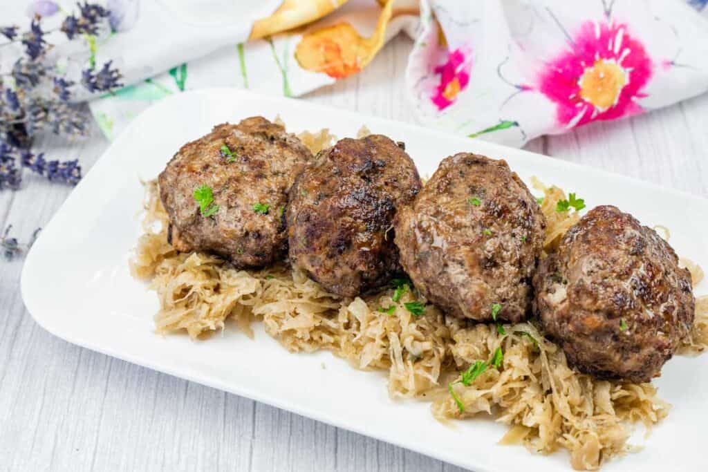 Four browned meat patties are served on a bed of shredded cabbage on a white plate.