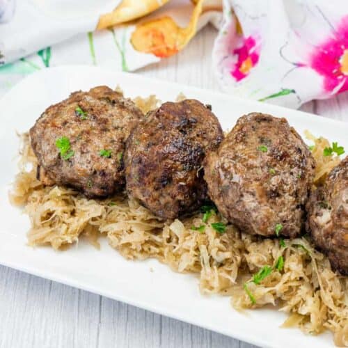 Four browned meat patties are served on a bed of shredded cabbage on a white plate.