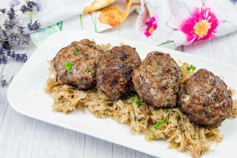 Four browned meat patties are served on a bed of shredded cabbage on a white plate.