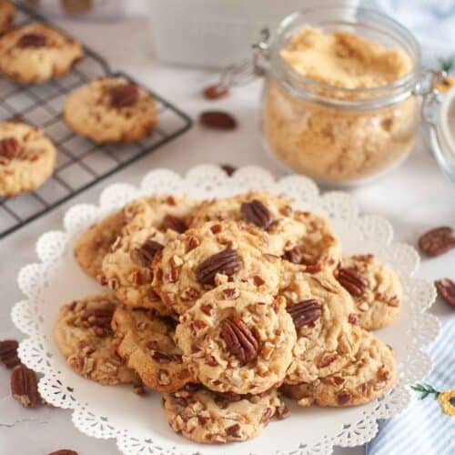 A plate of butter pecan cookies is beside the jar of sugar and other cookies on the cooling rack.