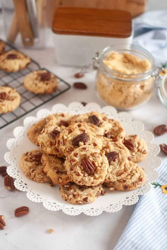 A plate of butter pecan cookies is beside the jar of sugar and other cookies on the cooling rack.