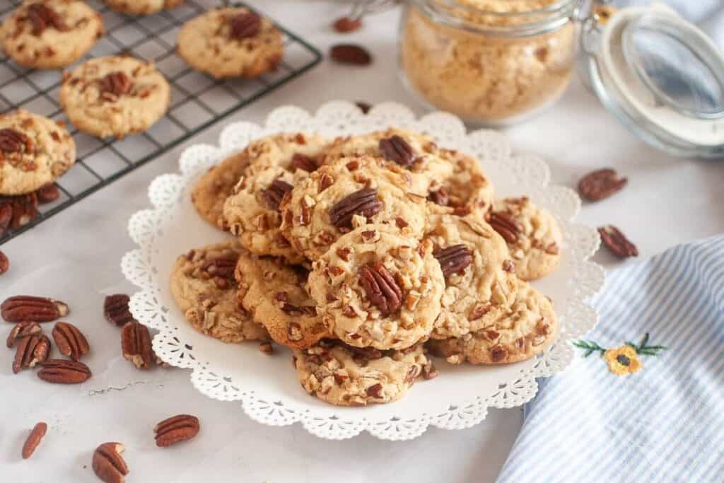 A plate of butter pecan cookies is placed near the cloth beside the jar of sugar and other cookies on the cooling rack.