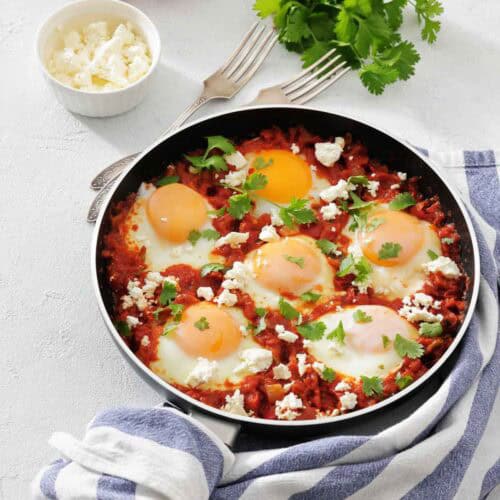 Pan-fried eggs with tomato sauce and feta cheese, garnished with cilantro.