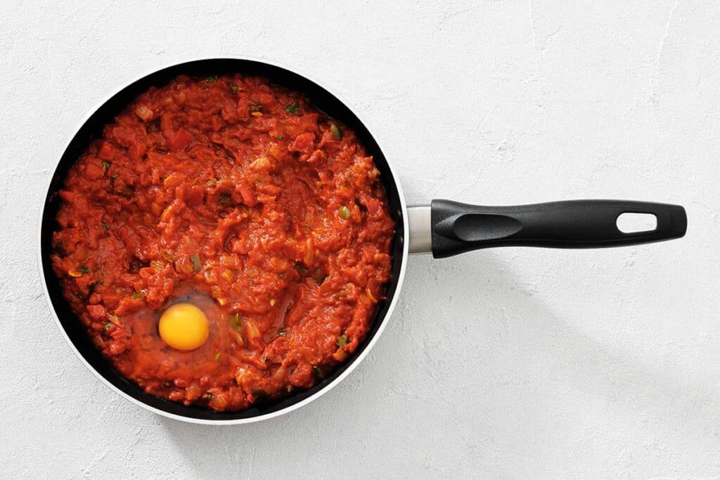 Savory tomato-based chili in a black skillet with a single poached egg. Perfect hearty dish for breakfast or dinner.