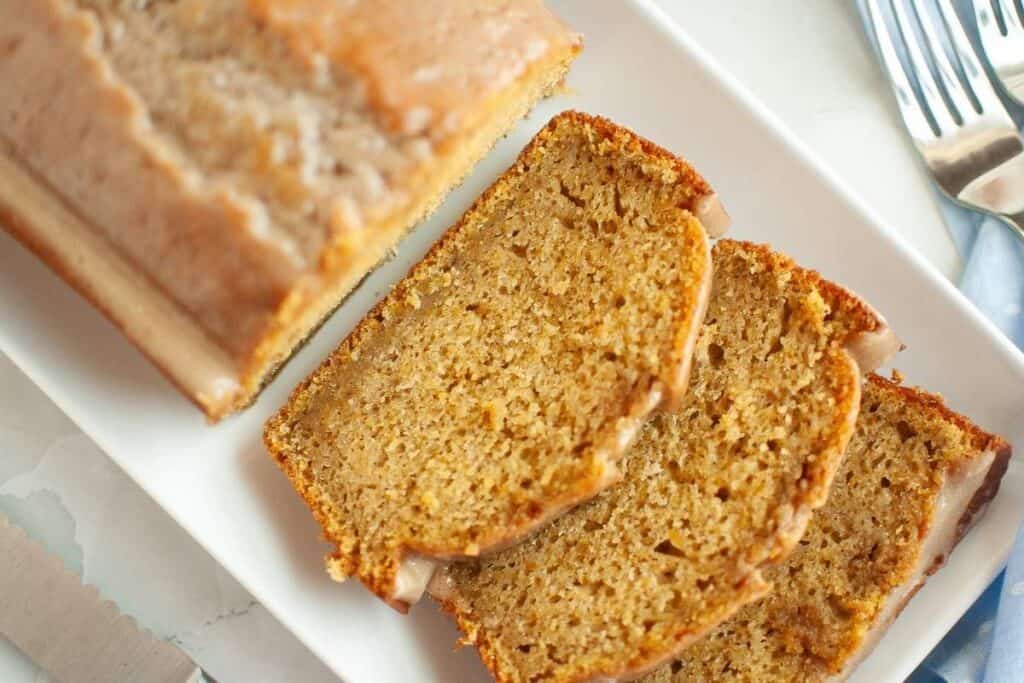 Three slices of Butternut Squash Loaf with Spiced Icing beside the remaining loaf bread on a plate.