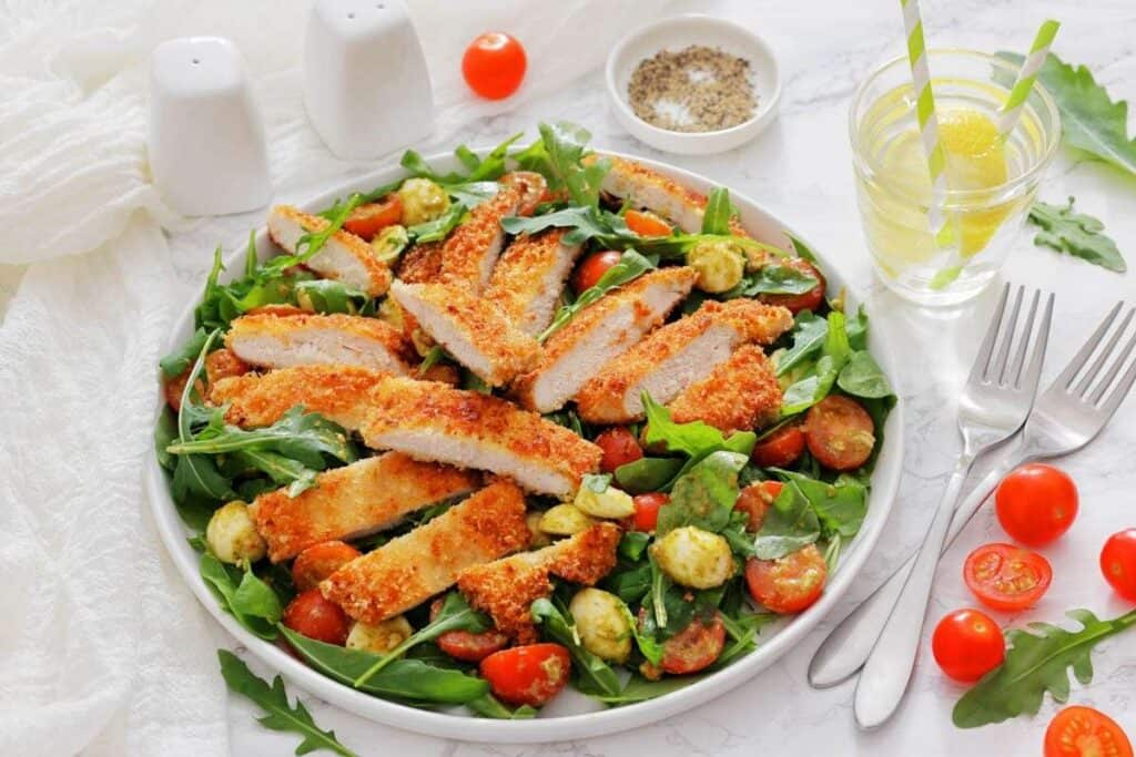 A white plate is filled with a vibrant Chicken Parmesan Salad beside two forks.