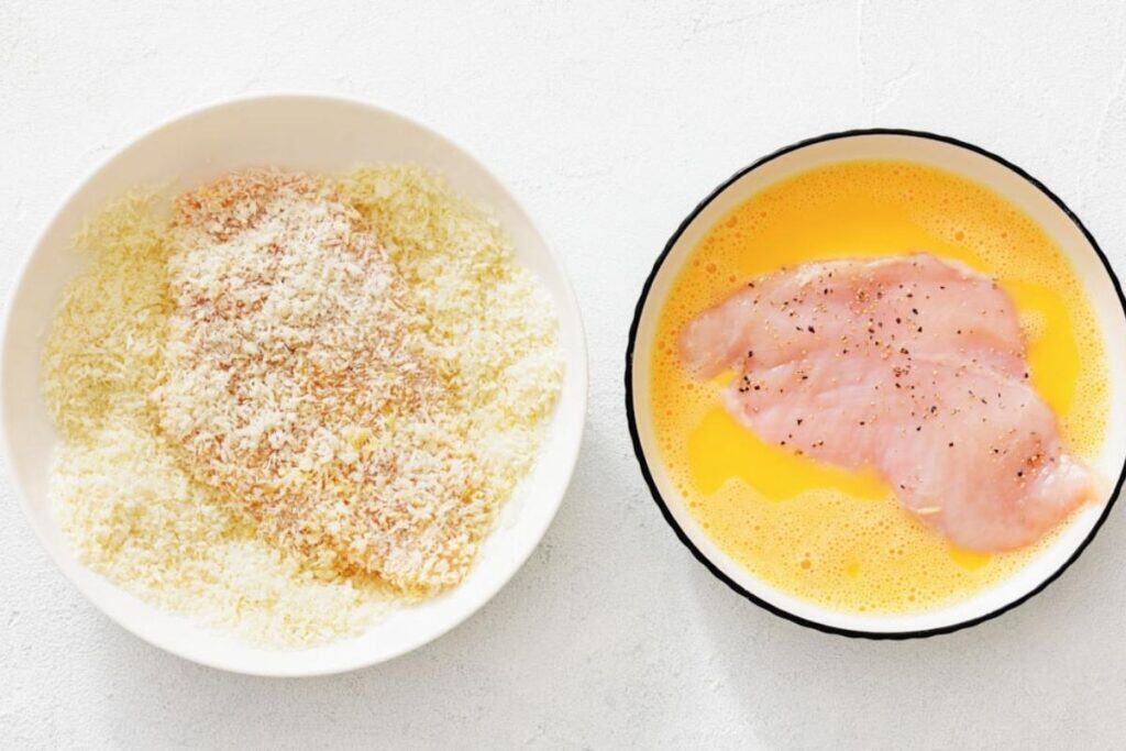 Chicken cutlets being dipped in egg and coated with panko, ready to fry for Chicken Parmesan Salad.