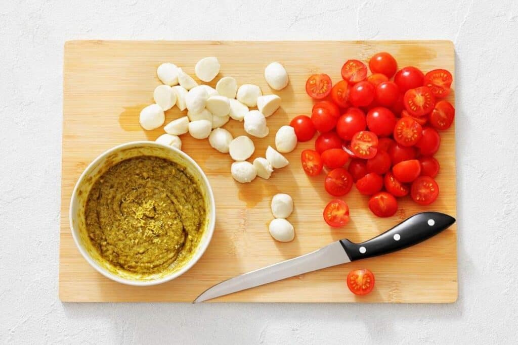 In a large bowl, pesto, lemon zest, and lemon juice are whisked into a dressing, ready to be tossed with cherry tomatoes, arugula, and bocconcini.