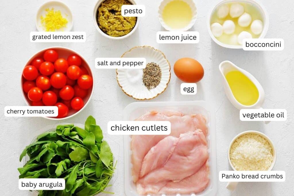 Ingredients for Chicken Parmesan Salad: chicken cutlets, egg, panko, salt and pepper, vegetable oil, pesto, lemon zest and juice, cherry tomatoes, arugula, and bocconcini ready to assemble.