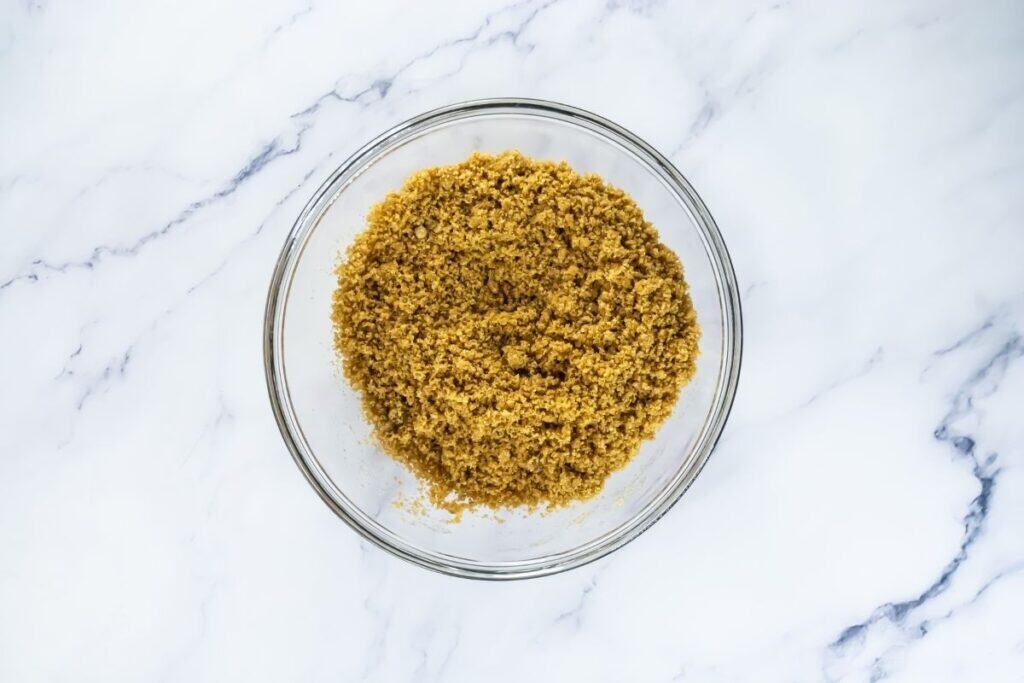 A glass bowl filled with light brown breadcrumbs on a white marble surface.