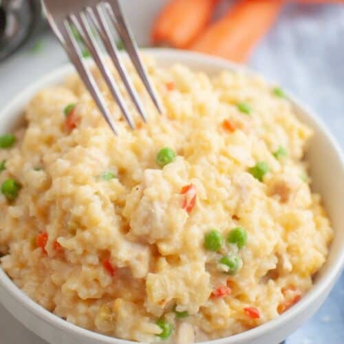 A fork is poised to take a portion of Slow Cooker Chicken and Rice from a white bowl.