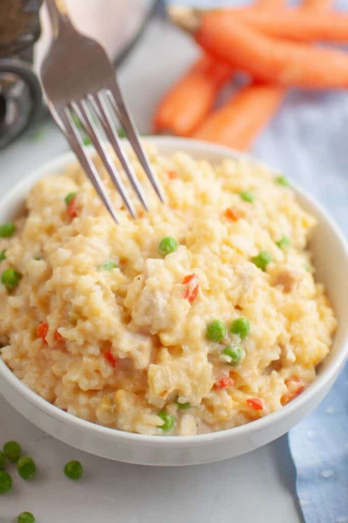 A fork is poised to take a portion of Slow Cooker Chicken and Rice from a white bowl.