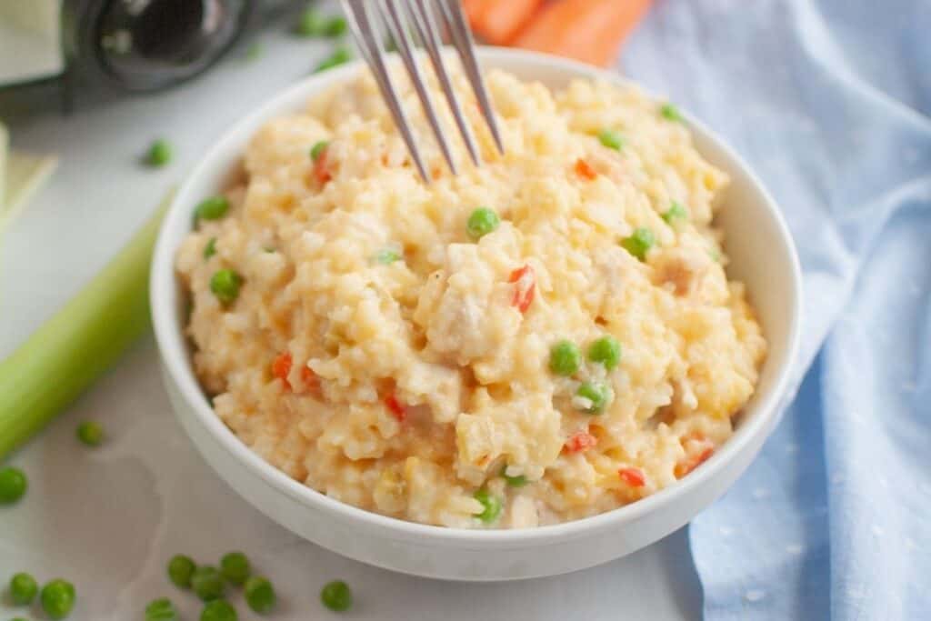 A fork is poised to take a portion of Slow Cooker Chicken and Rice from a white bowl.