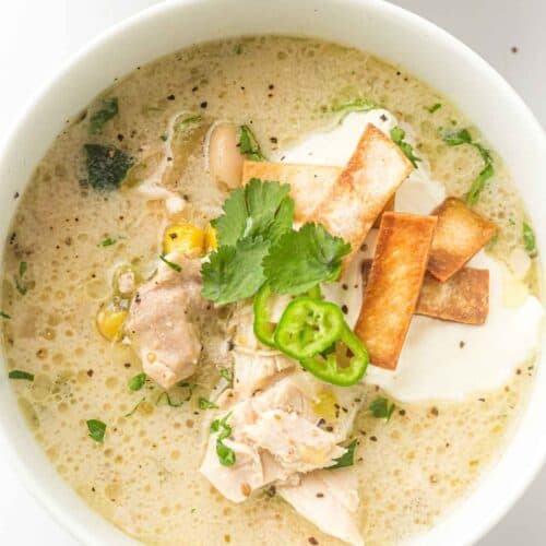 The creamy slow cooker chicken chili sits warm in a white bowl, showing off its rich, velvety texture with tender chicken, hearty beans, and pops of corn and green chilies.