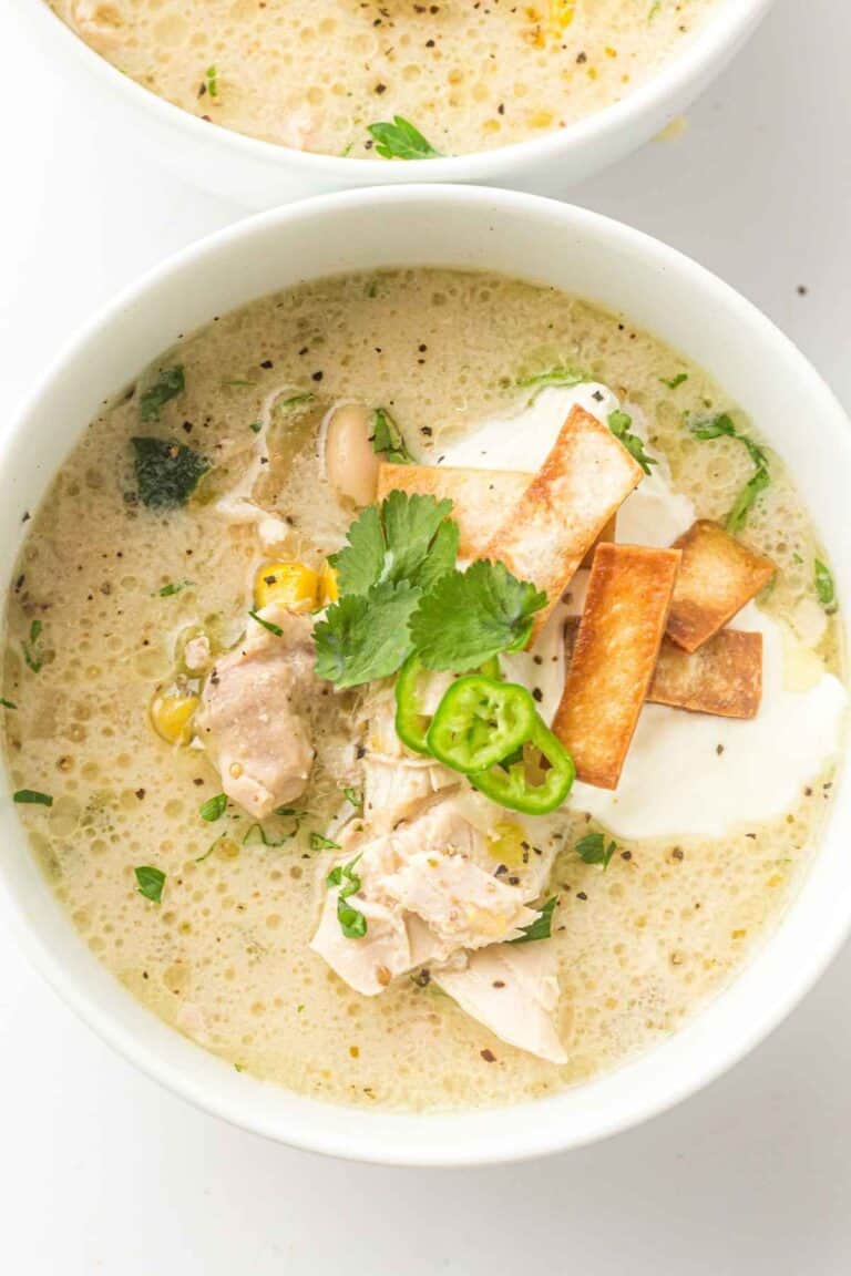 The creamy slow cooker chicken chili sits warm in a white bowl, showing off its rich, velvety texture with tender chicken, hearty beans, and pops of corn and green chilies.