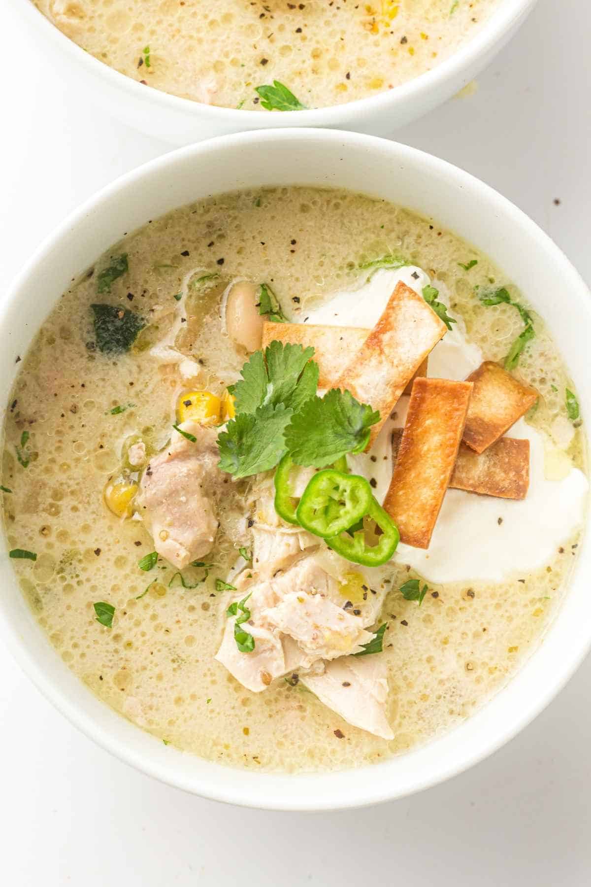 The creamy slow cooker chicken chili sits warm in a white bowl, showing off its rich, velvety texture with tender chicken, hearty beans, and pops of corn and green chilies.