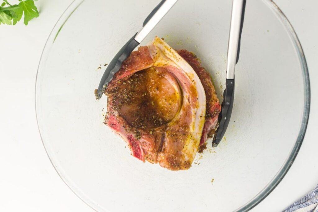 Juicy pork in a glass bowl with herbs and spices, ready to cook, showcasing flavorful preparation for optimal taste.