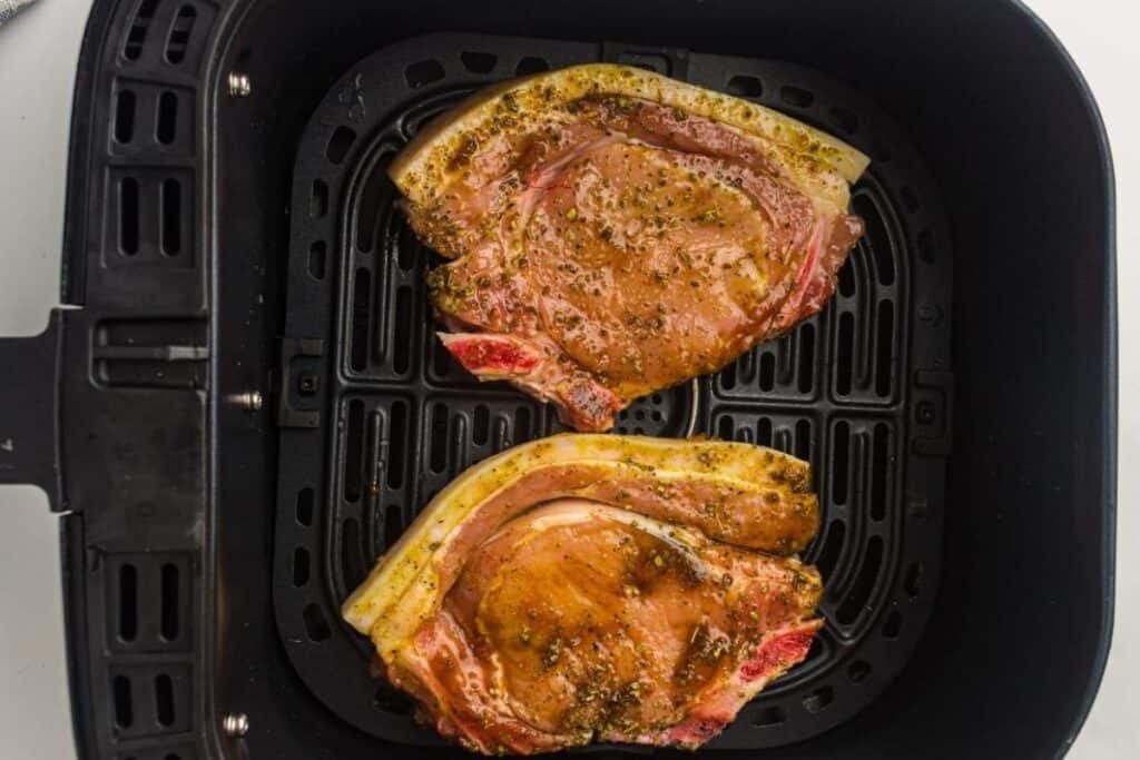 pork chops seasoned with herbs and spices, cooking in an air fryer for a quick, flavorful dish.