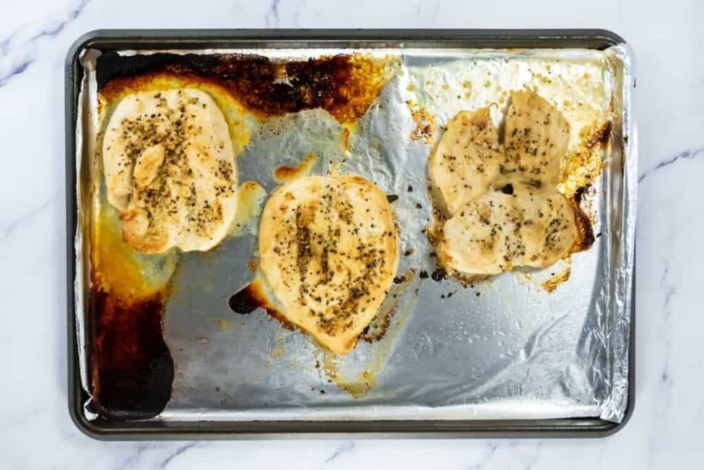 Delicious baked garlic chicken breasts topped with herbs, served on a foil-lined tray for easy cleanup.