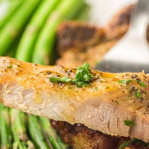 Juicy grilled chicken breast garnished with herbs, served with fresh asparagus and roasted vegetables.