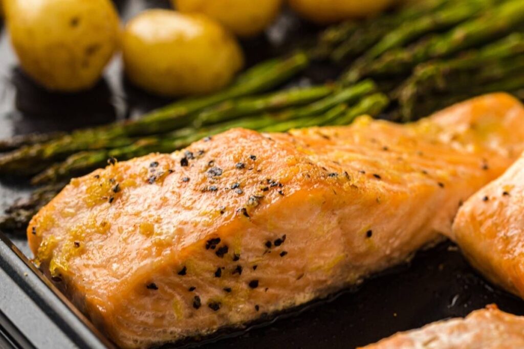 A close up sheet-pan dinner with flaky salmon, tender asparagus, and golden roasted potatoes, finished with fresh lemon for a bright, savory touch.
