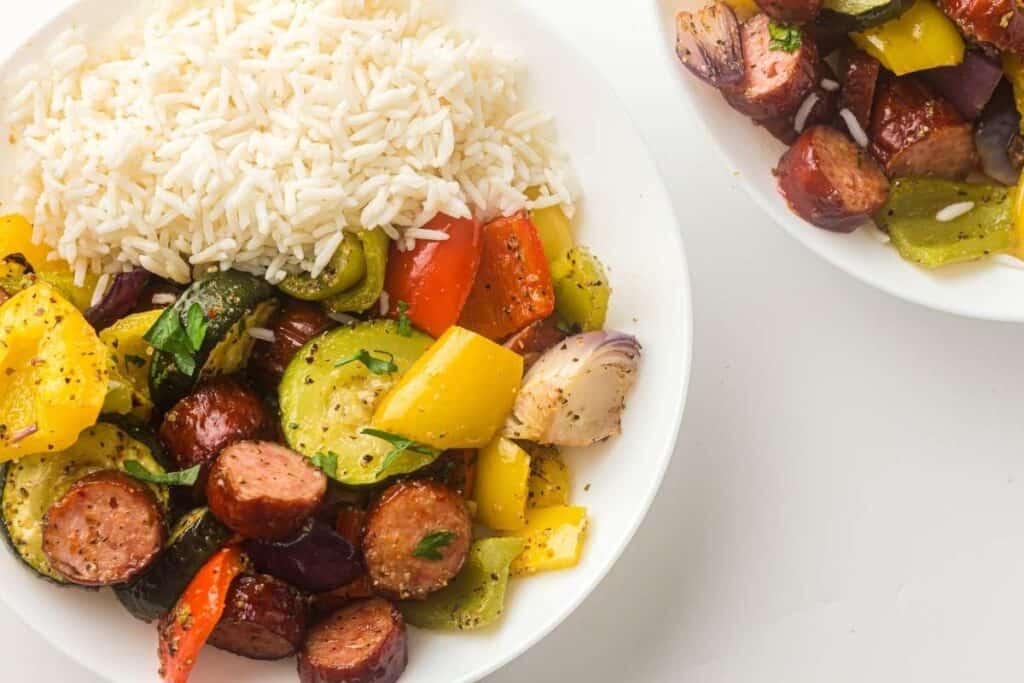 A white plate with Sheet Pan Sausage & Roasted Vegetables and rice.