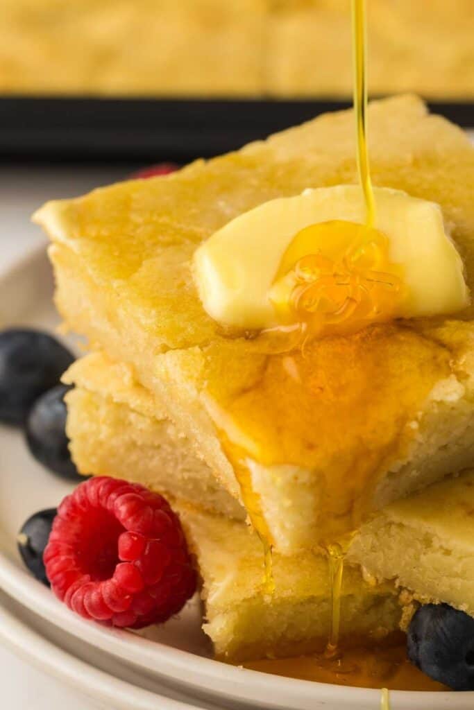 A plate of stackable sheet pan pancakes topped with butter, honey, and berries.