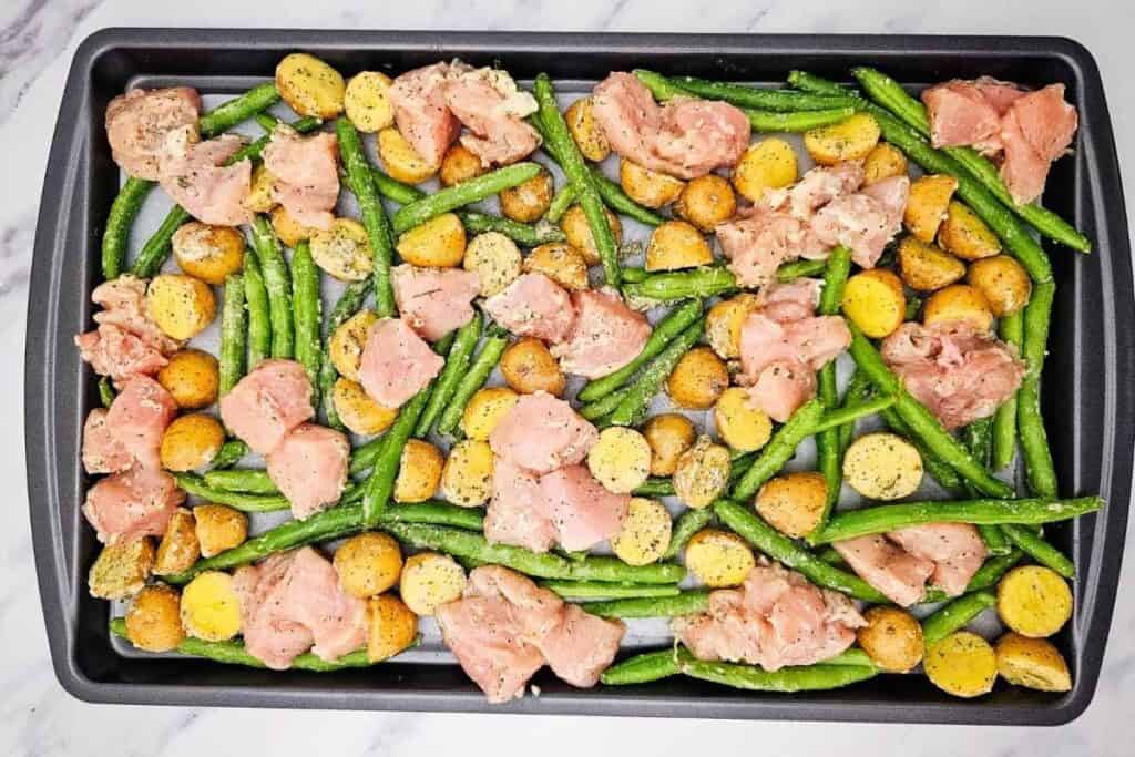 Freshly prepared chicken, green beans, and roasted potatoes on a baking sheet.