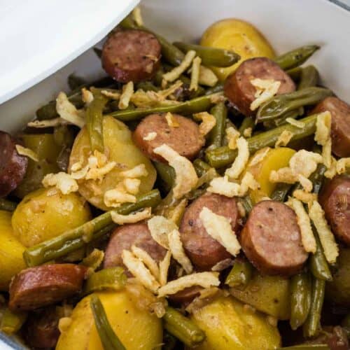 A bowl of Swamp Potatoes with cooked green beans, sliced sausage, and halved potatoes, topped with crispy fried onions.