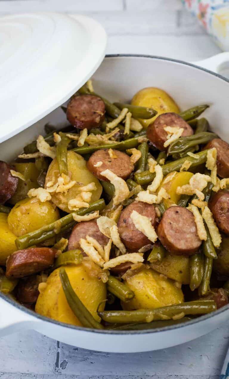 A bowl of Swamp Potatoes with cooked green beans, sliced sausage, and halved potatoes, topped with crispy fried onions.