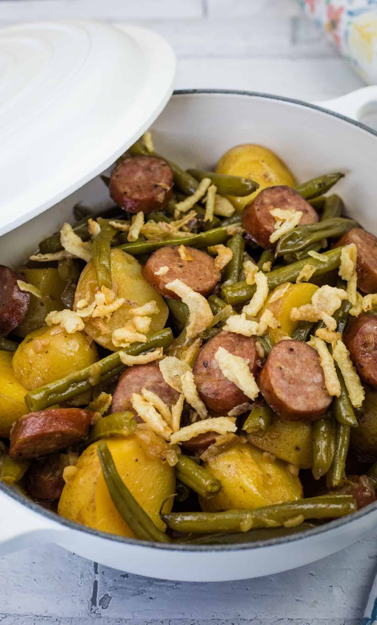 A bowl of Swamp Potatoes with cooked green beans, sliced sausage, and halved potatoes, topped with crispy fried onions.