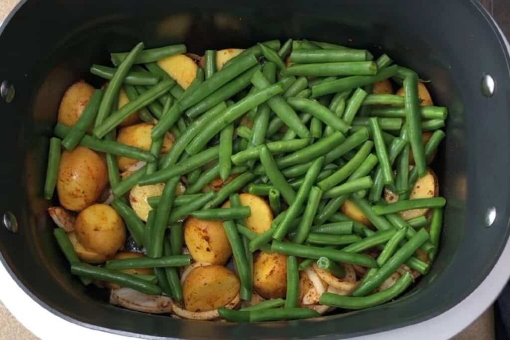 This image shows green beans and baby potatoes being cooked together in a black pot, highlighting fresh ingredients and healthy cooking.
