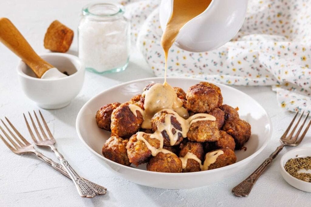 A white plate filled with Swedish meatballs, topped with rich gravy flowing from the sauce.