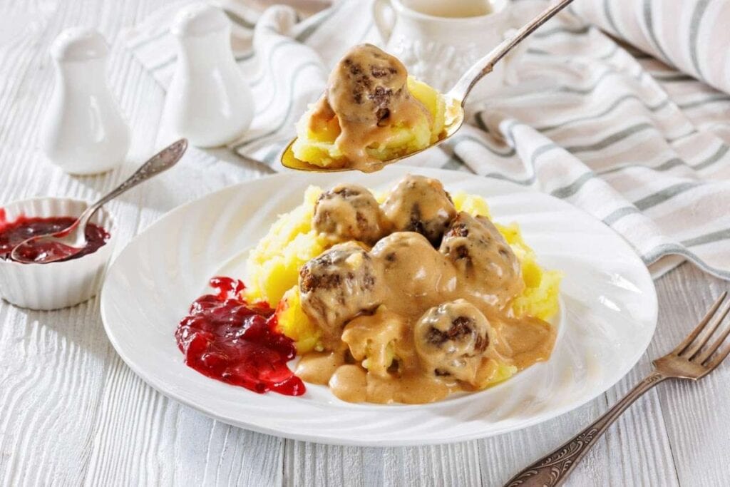 A spoon lifting a serving of Swedish meatballs covered in gravy.