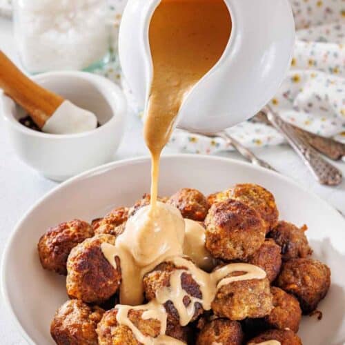 A white plate filled with Swedish meatballs, topped with rich gravy flowing from the sauce.