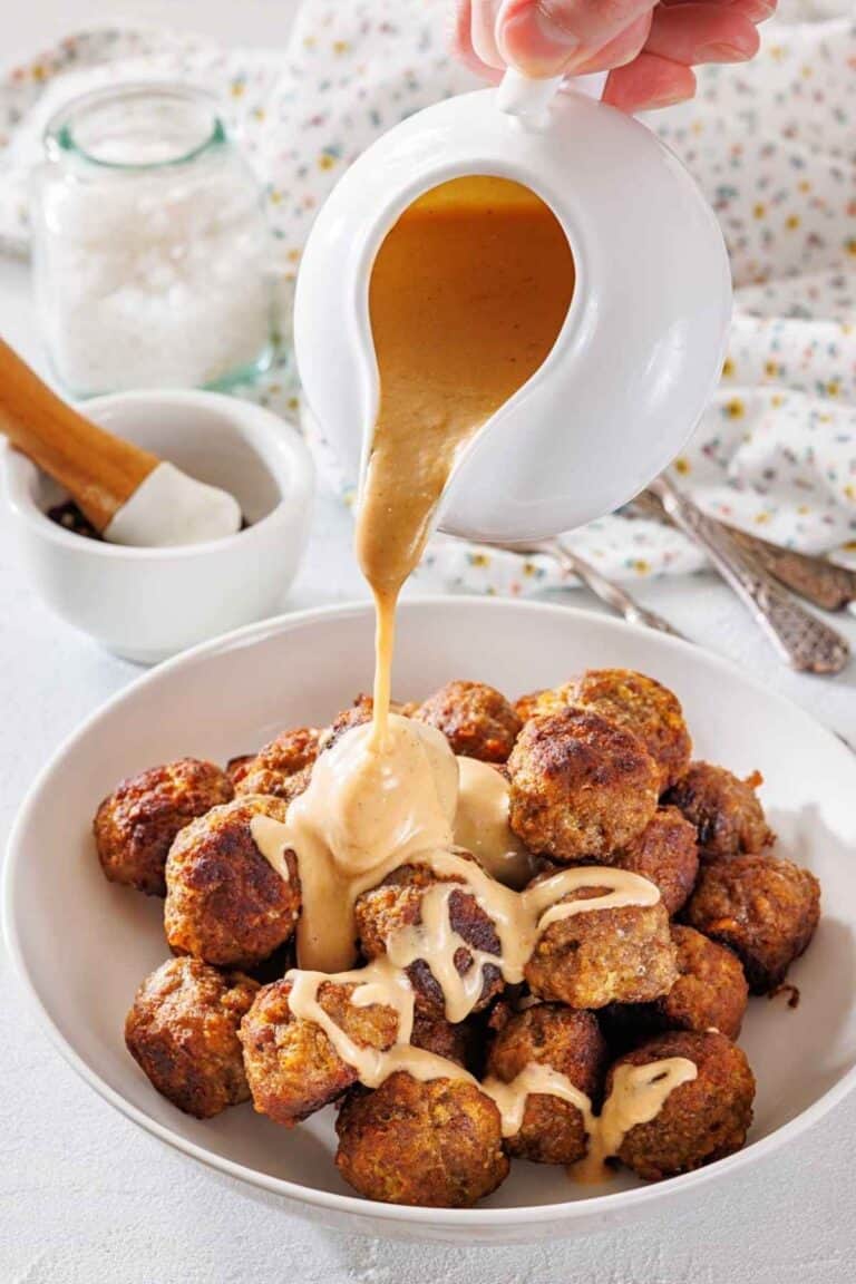 A white plate filled with Swedish meatballs, topped with rich gravy flowing from the sauce.